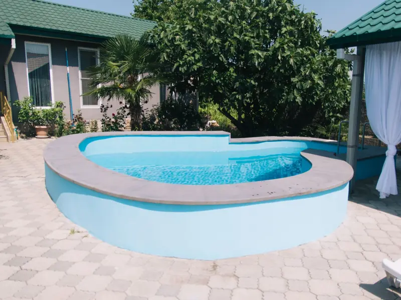 Backyard swimming pool and patio beside a home with palm trees